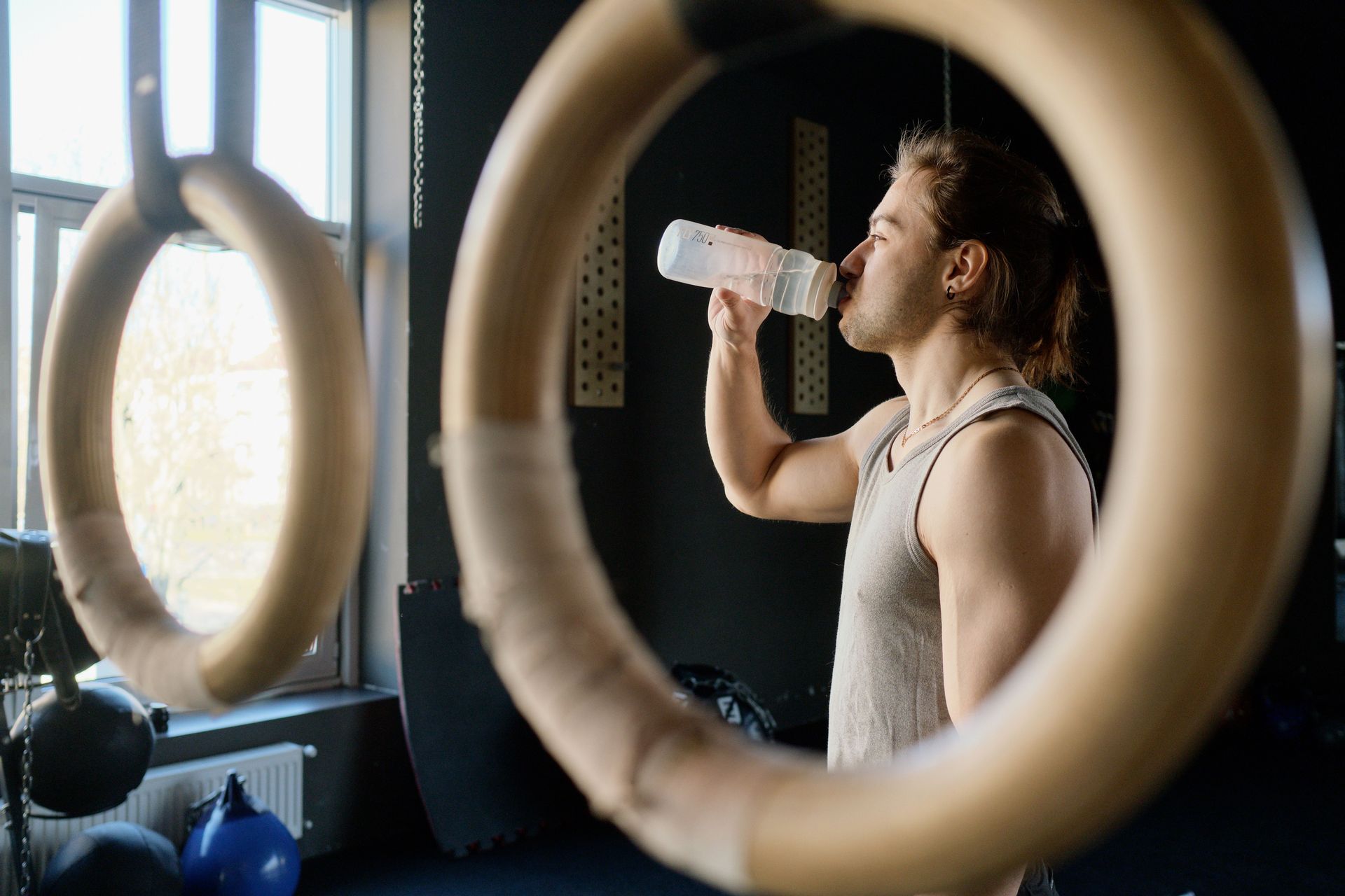 Person drinks water from a bottle in a gym, framed by large circular rings