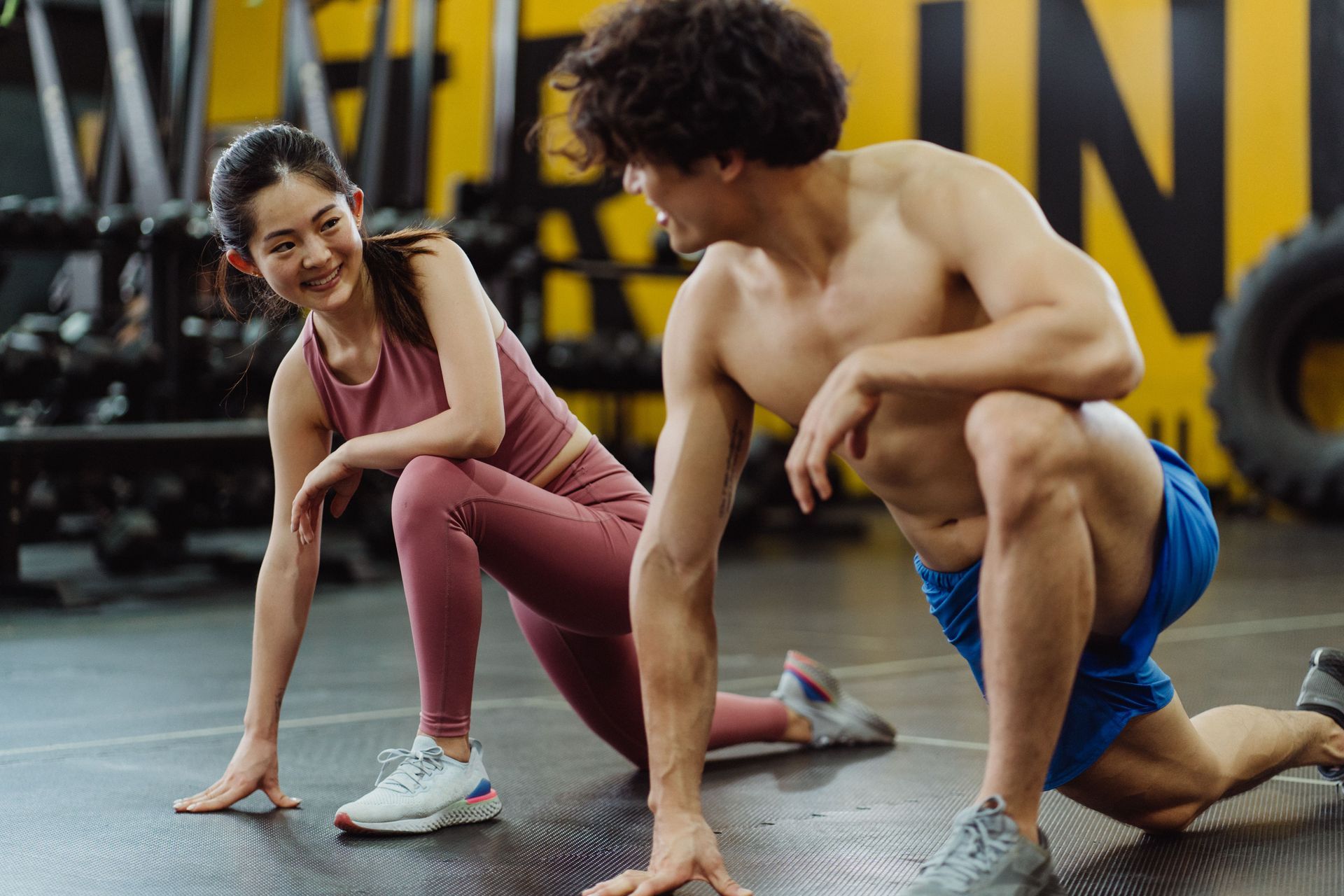 Two athletes stretching on a gym floor, smiling during a workout session