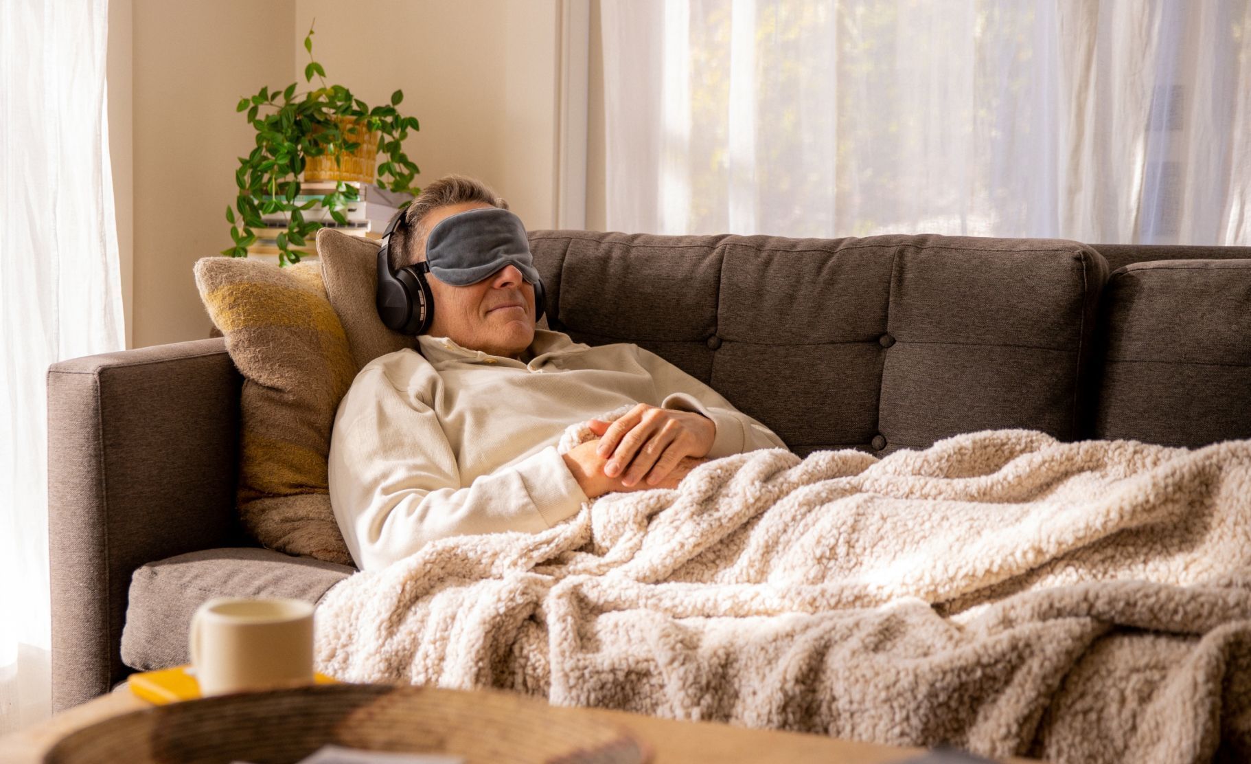 A man is laying on a couch wearing a sleep mask and headphones.