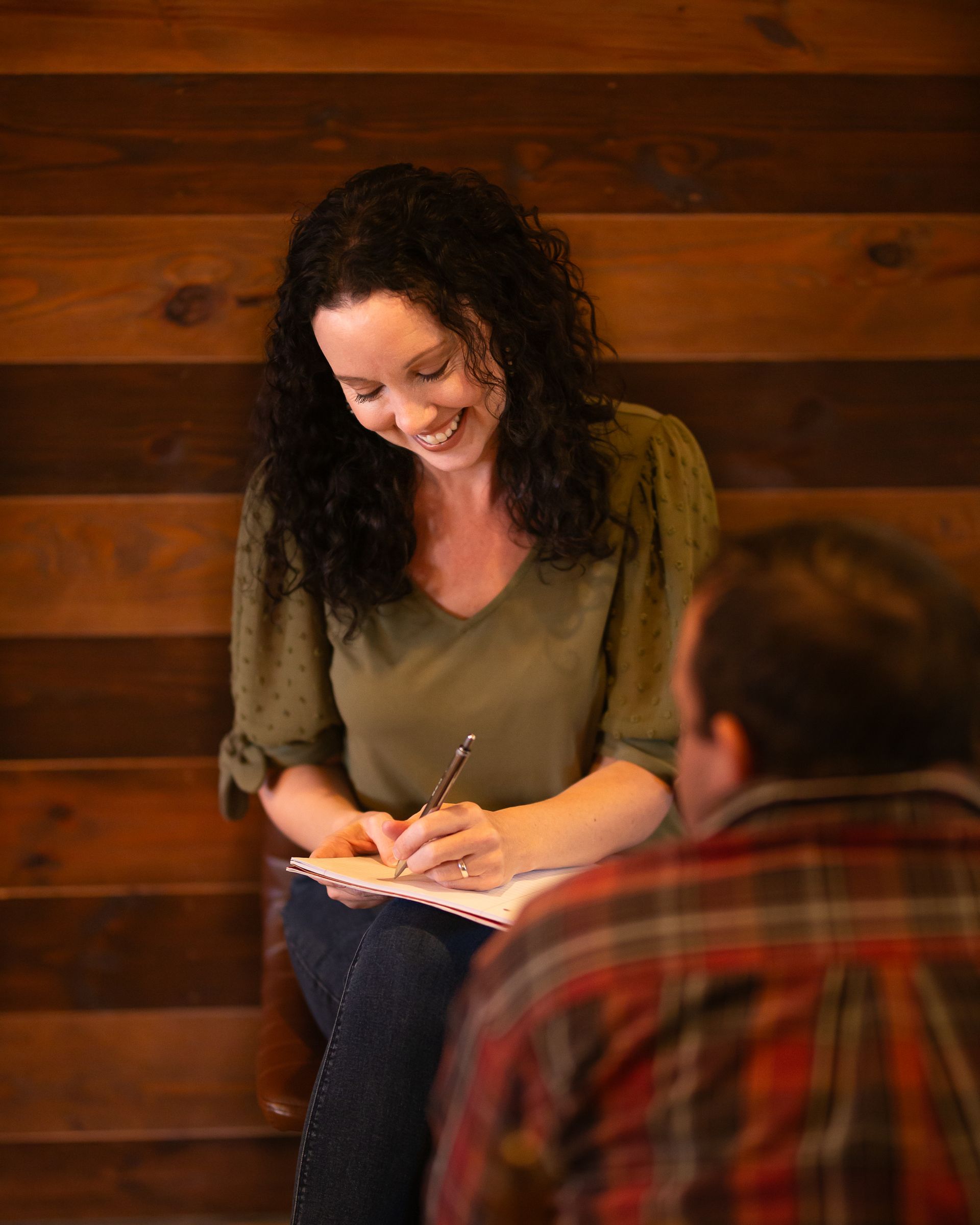 A woman is writing in a notebook while sitting next to a man.