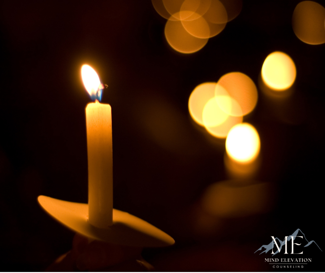 A lit candle in a dark room with a mtn elevation logo in the background