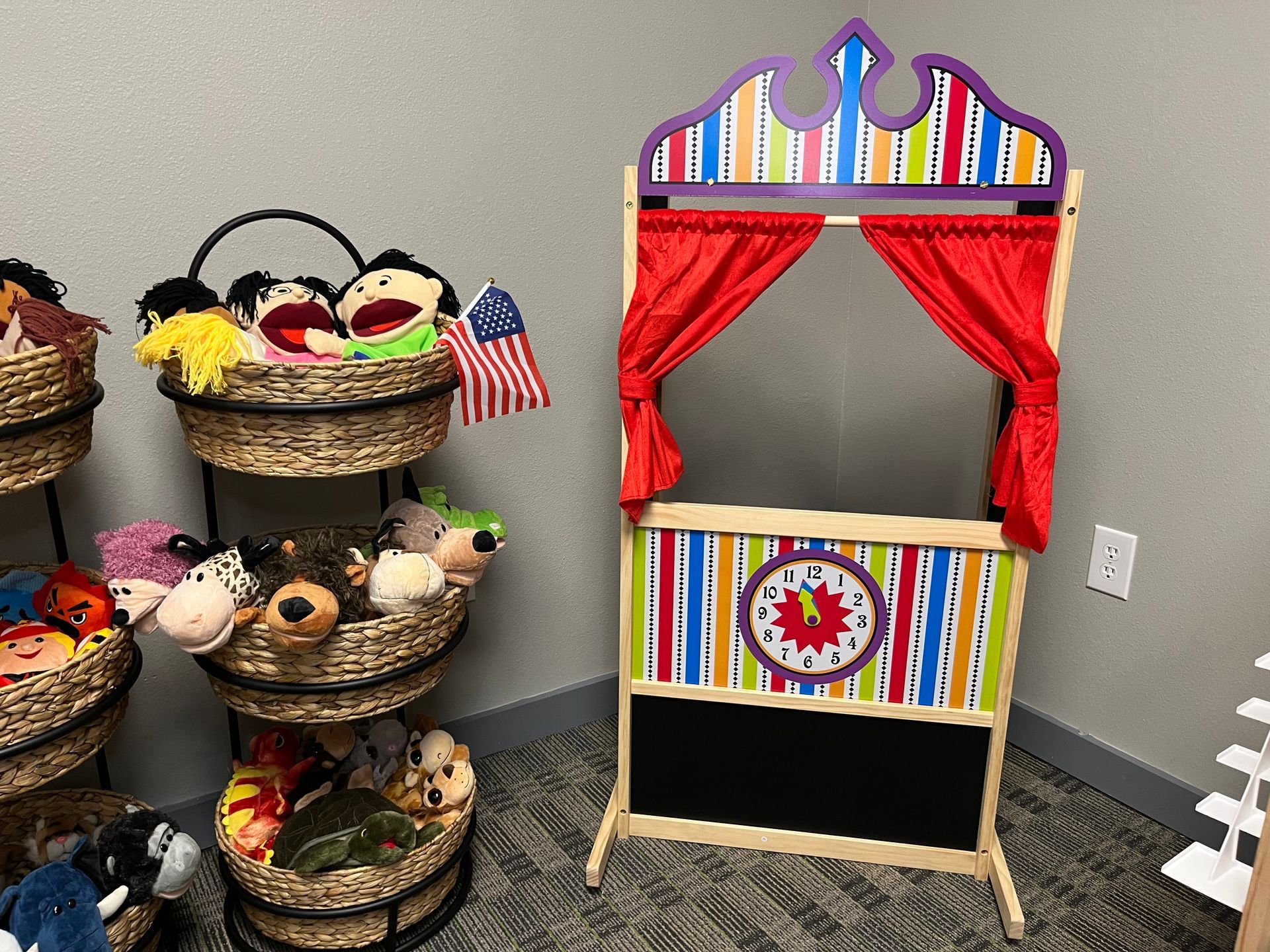 A puppet theater is sitting next to a stack of baskets filled with stuffed animals.