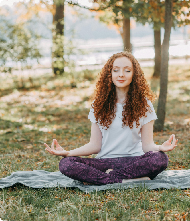 A woman is sitting on a blanket in a lotus position with her eyes closed.