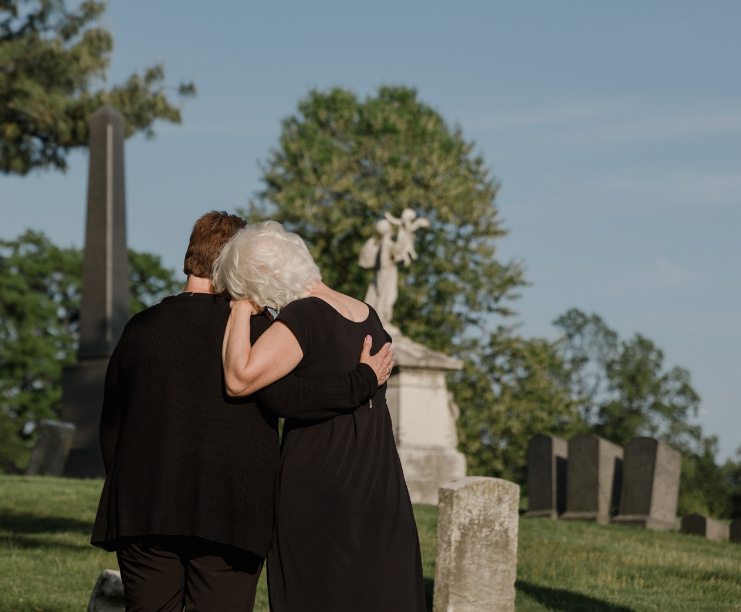 Two women are hugging each other in a cemetery.