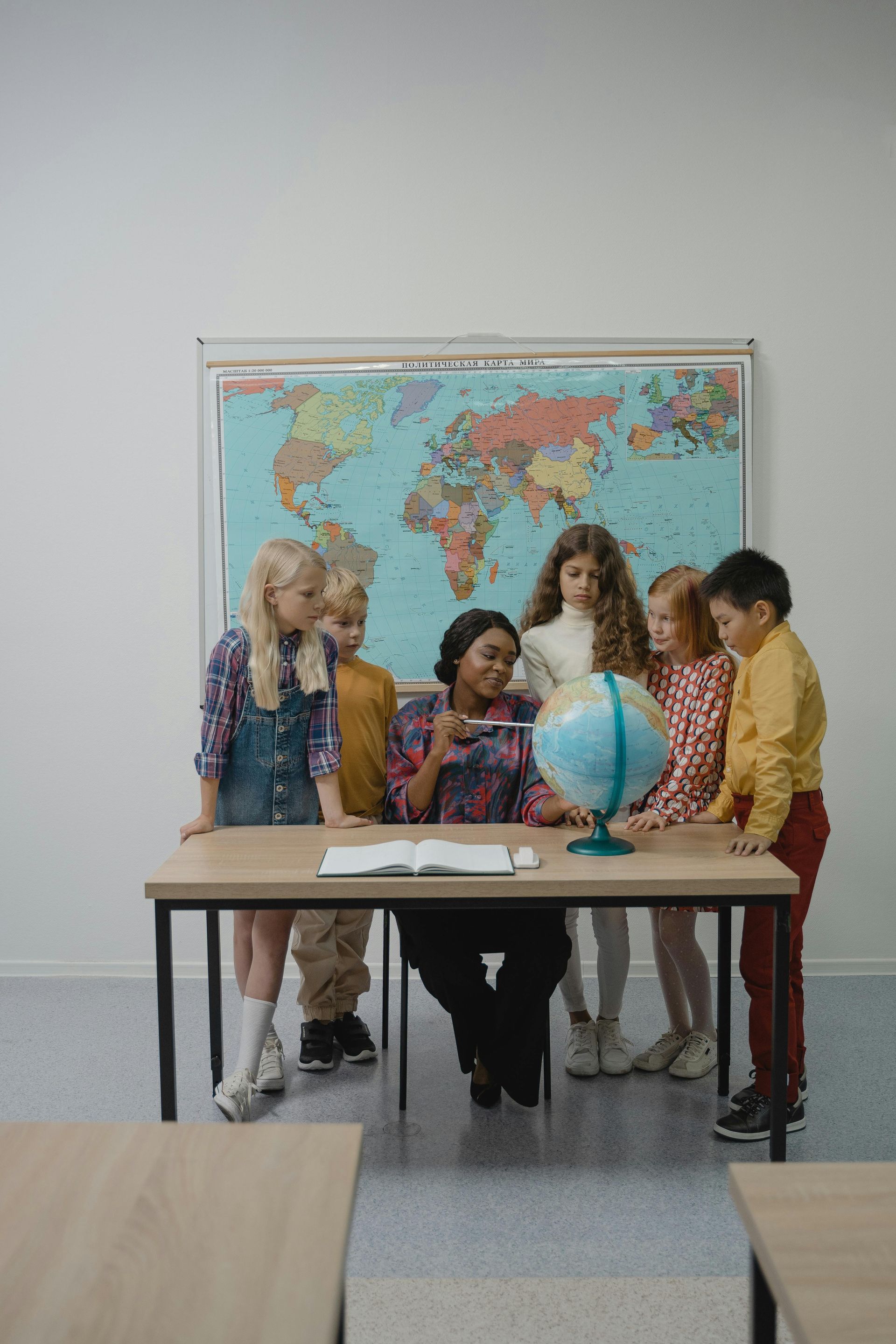 A group of children are sitting at a table in front of a map of the world.