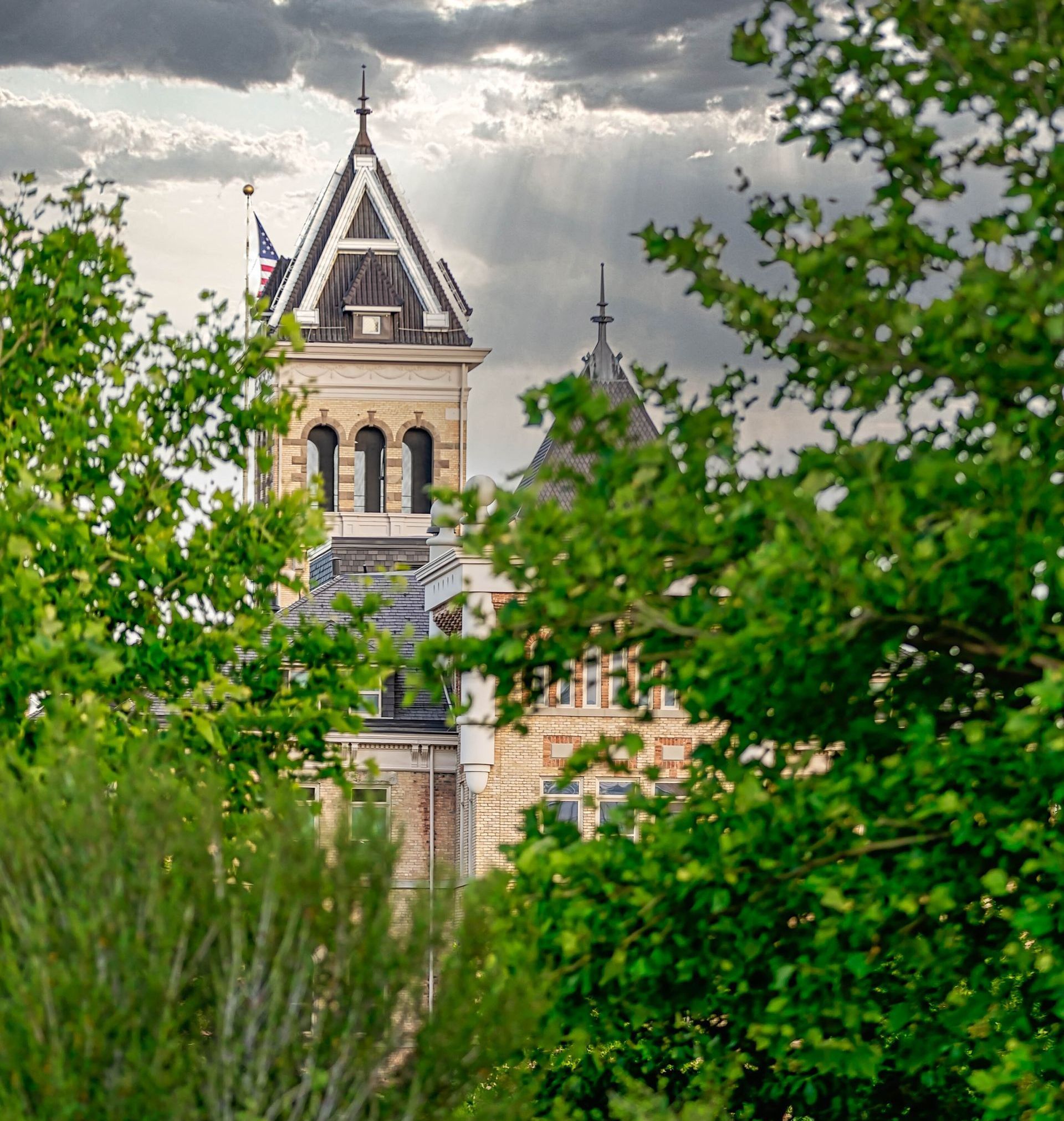 A large building with a steeple is surrounded by trees on a cloudy day.