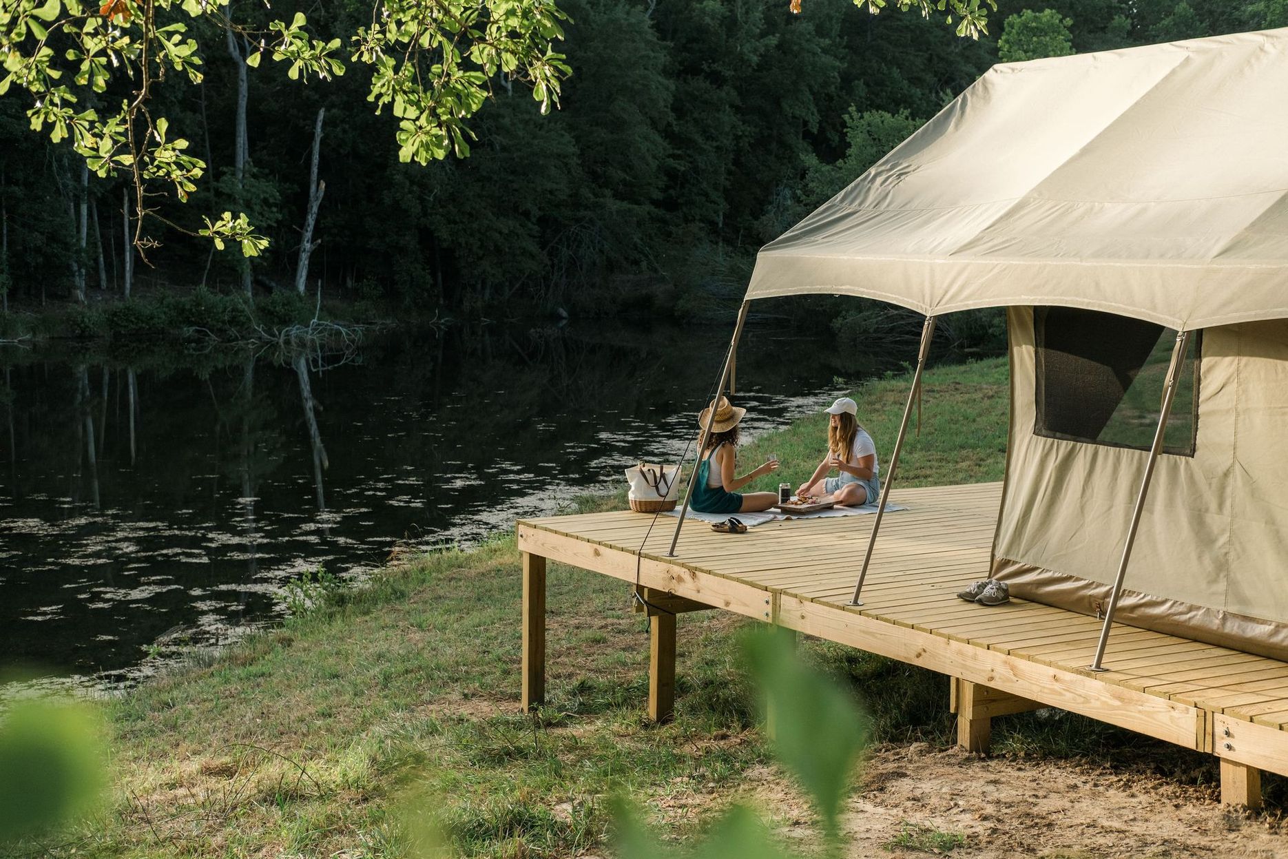 Two people are sitting on a dock next to a tent.