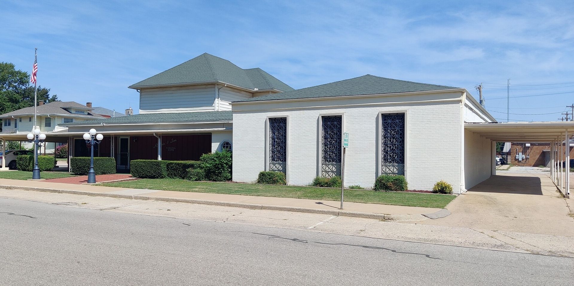 A white building with a green roof and three arched windows with black bars. A carport is on the right.