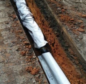 A white pipe is sitting in the dirt next to a brick wall.