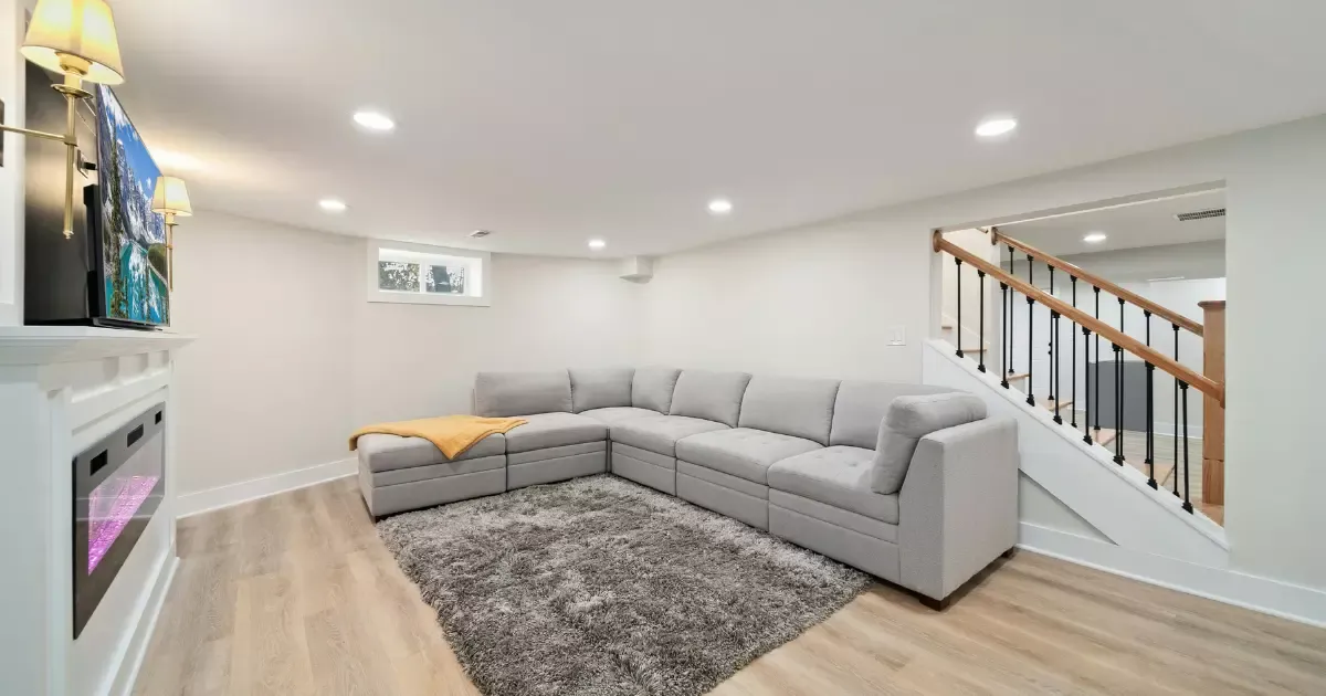 Finished basement living area with sectional sofa, electric fireplace, and modern staircase railing