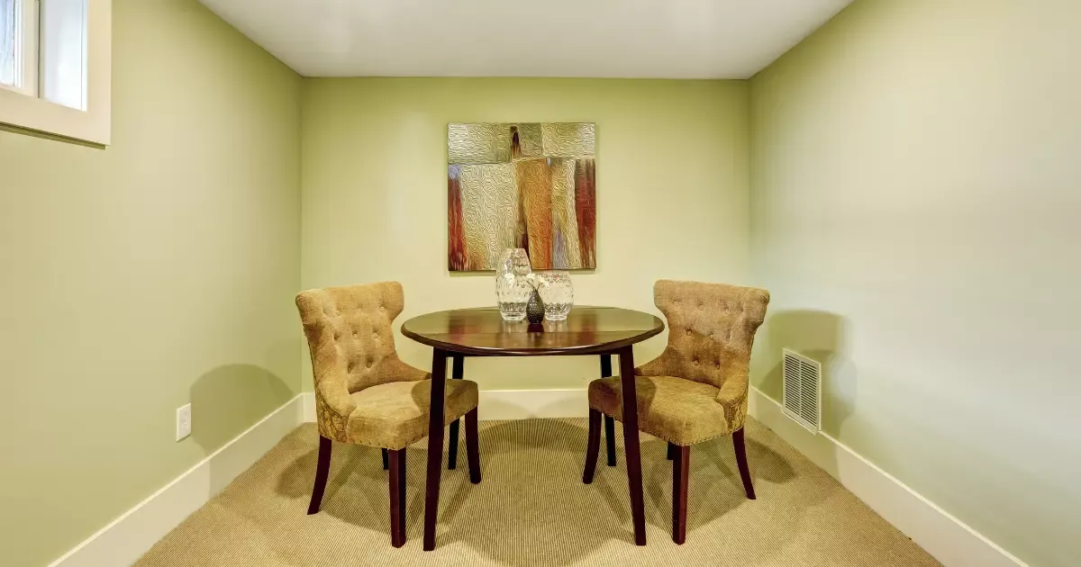 Small basement family room setup with round table and upholstered chairs in a bright corner