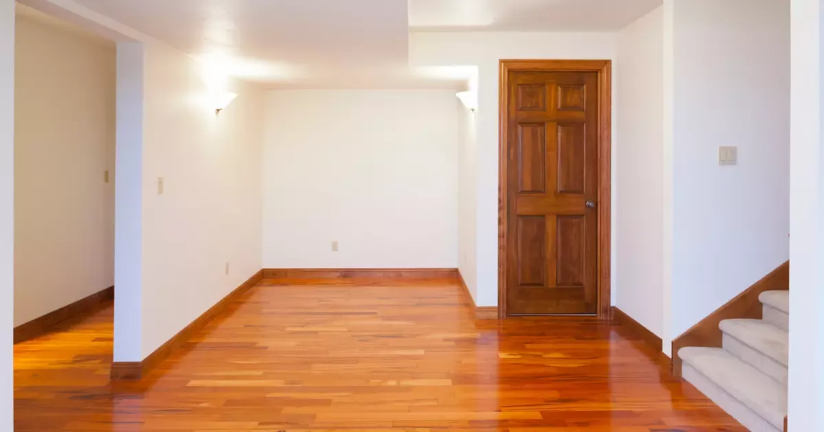 Bright open room with hardwood floors and wood door showcasing clean basement finishing design