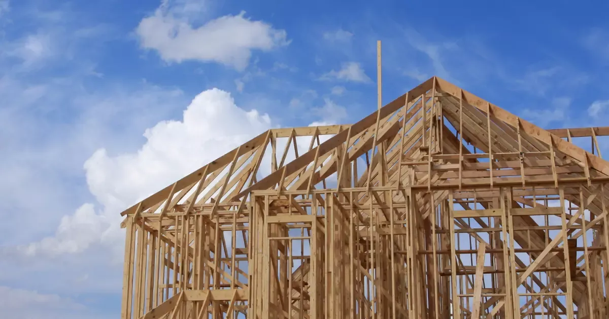 Custom home builder framing new house structure with wooden beams under blue sky