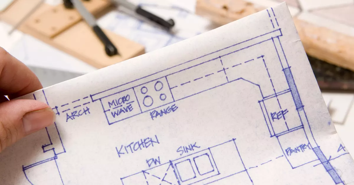 Close-up of a hand holding a kitchen layout blueprint during a home remodeling project