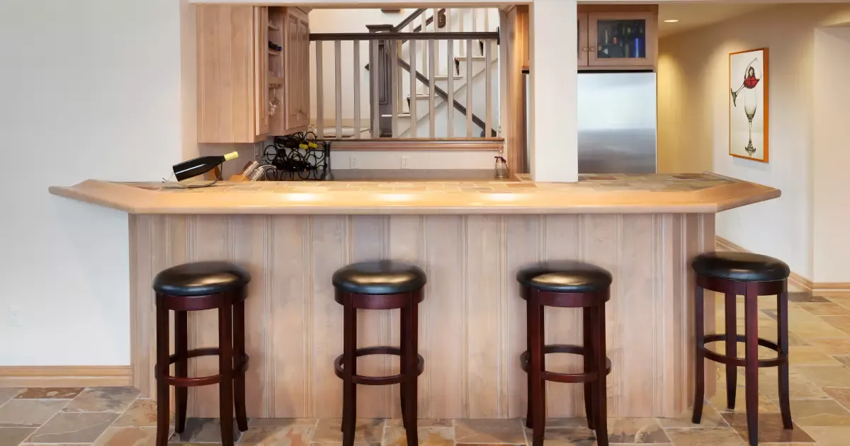 Basement remodeling with custom bar, wood cabinetry, tiled floor, and seating for four stools