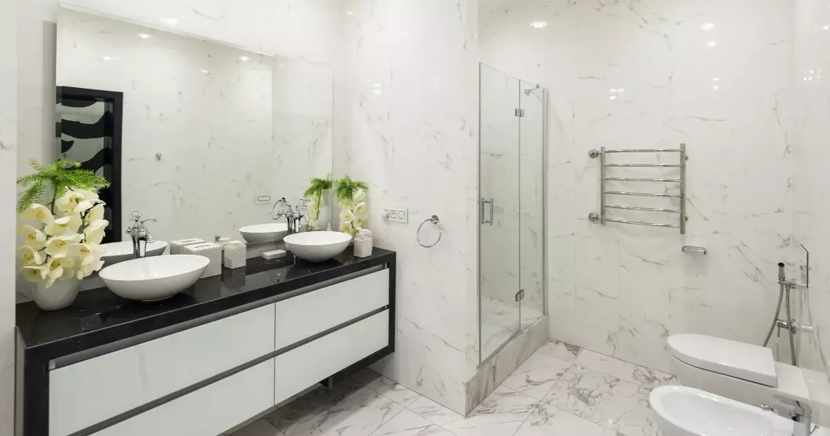 Modern basement bathroom with white marble walls, double vessel sinks, glass shower, and sleek chrome fixtures