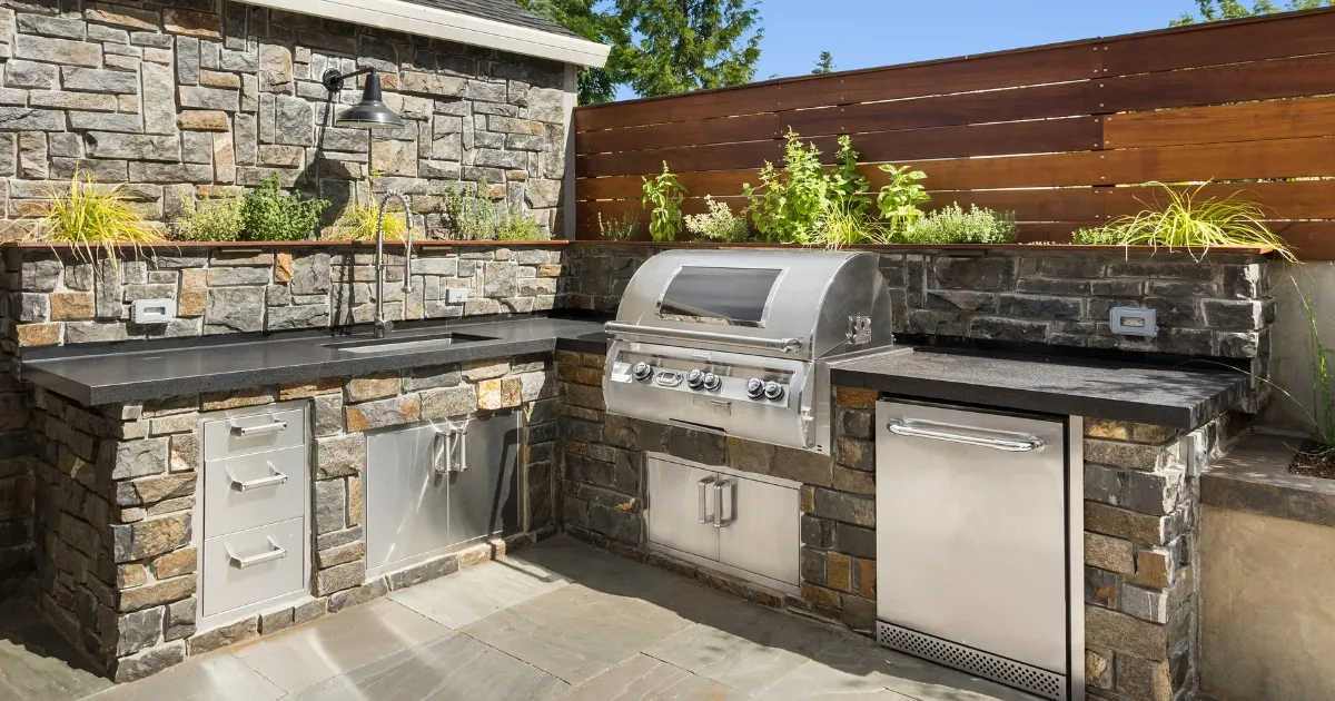 Custom stone outdoor kitchen with built-in grill, sink, storage, and modern stainless steel appliances