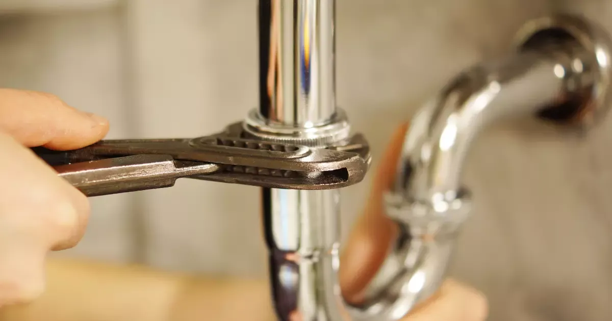 Close-up of plumber tightening chrome drain pipe under a sink during a basement bathroom installation