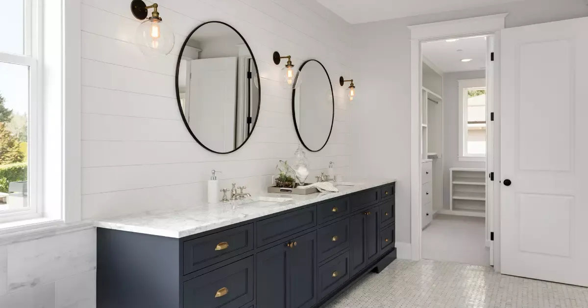 Bright white bathroom with double navy vanity, round mirrors, and marble countertop, bathroom remodeling design