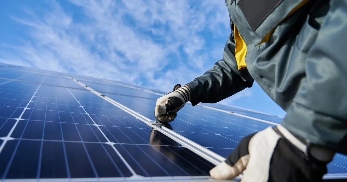 Technician inspecting and securing solar panels on a rooftop under a bright blue sky