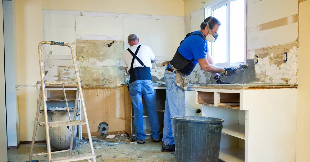 Two workers removing old kitchen cabinets and tiles during interior home construction renovation project