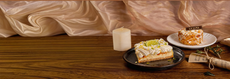 Desserts on plates with a glass of milk on a wooden table against a beige backdrop