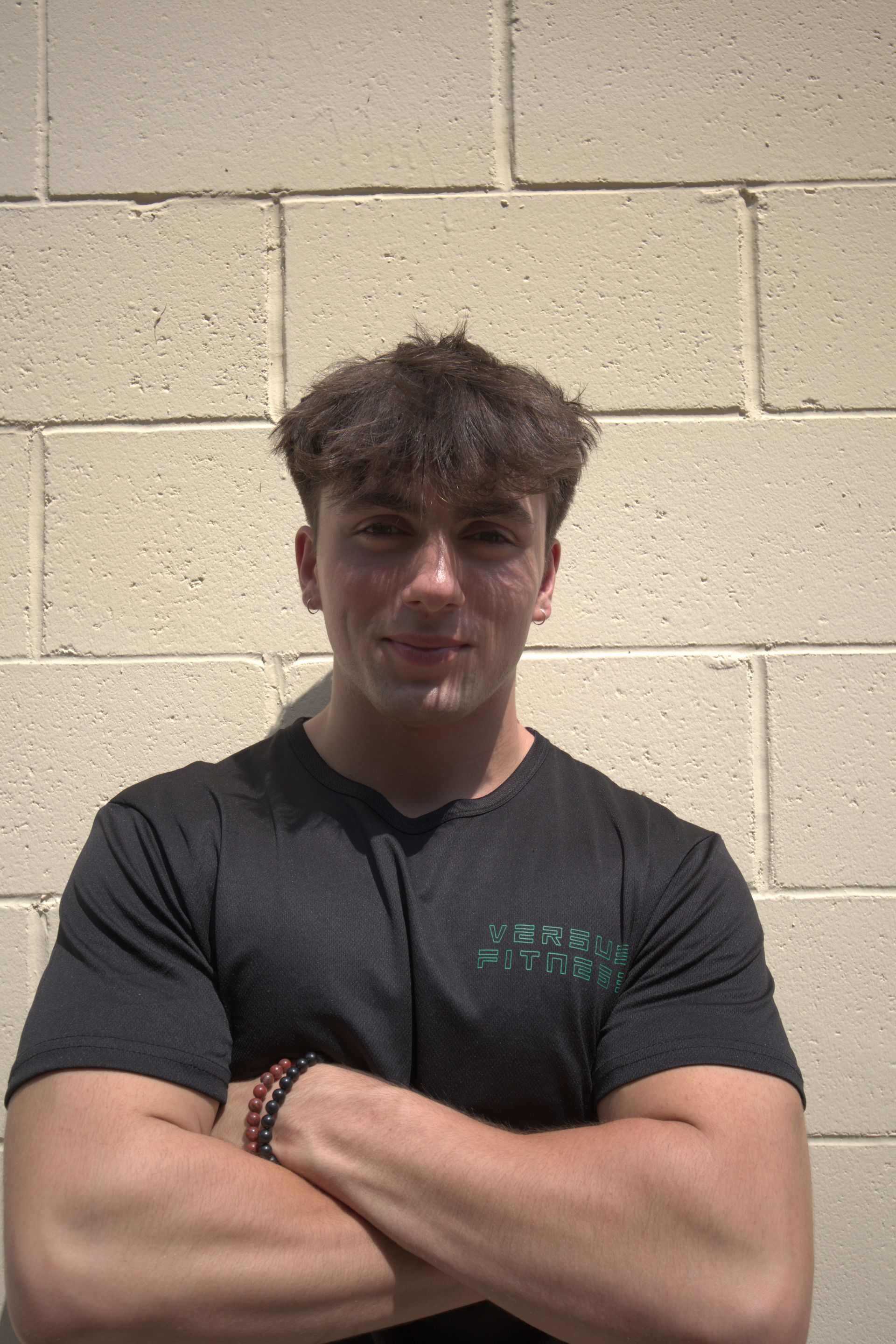 A smiling person in a black graphic t-shirt poses with a closed fist against a backdrop with metallic gold text.