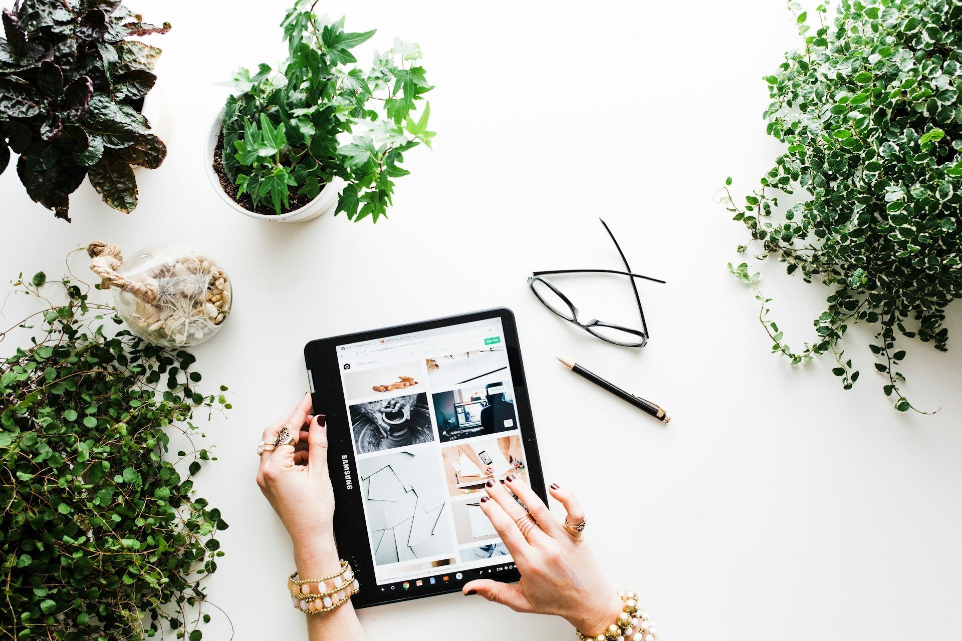 A woman is using a tablet computer on a table surrounded by potted plants.
