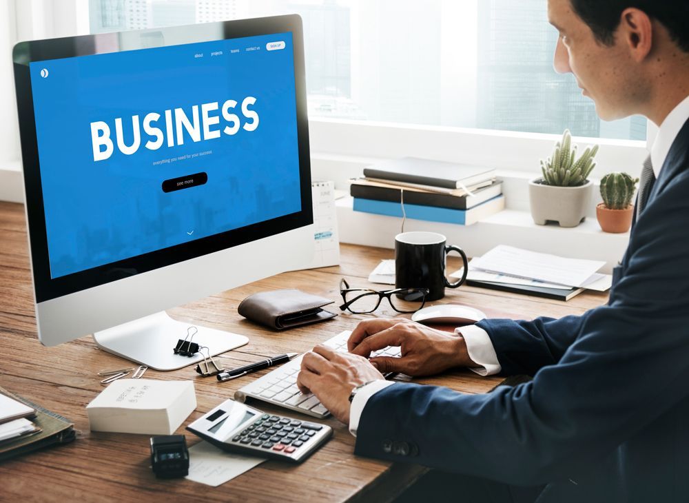 A man is sitting at a desk in front of a computer with the word business on the screen.