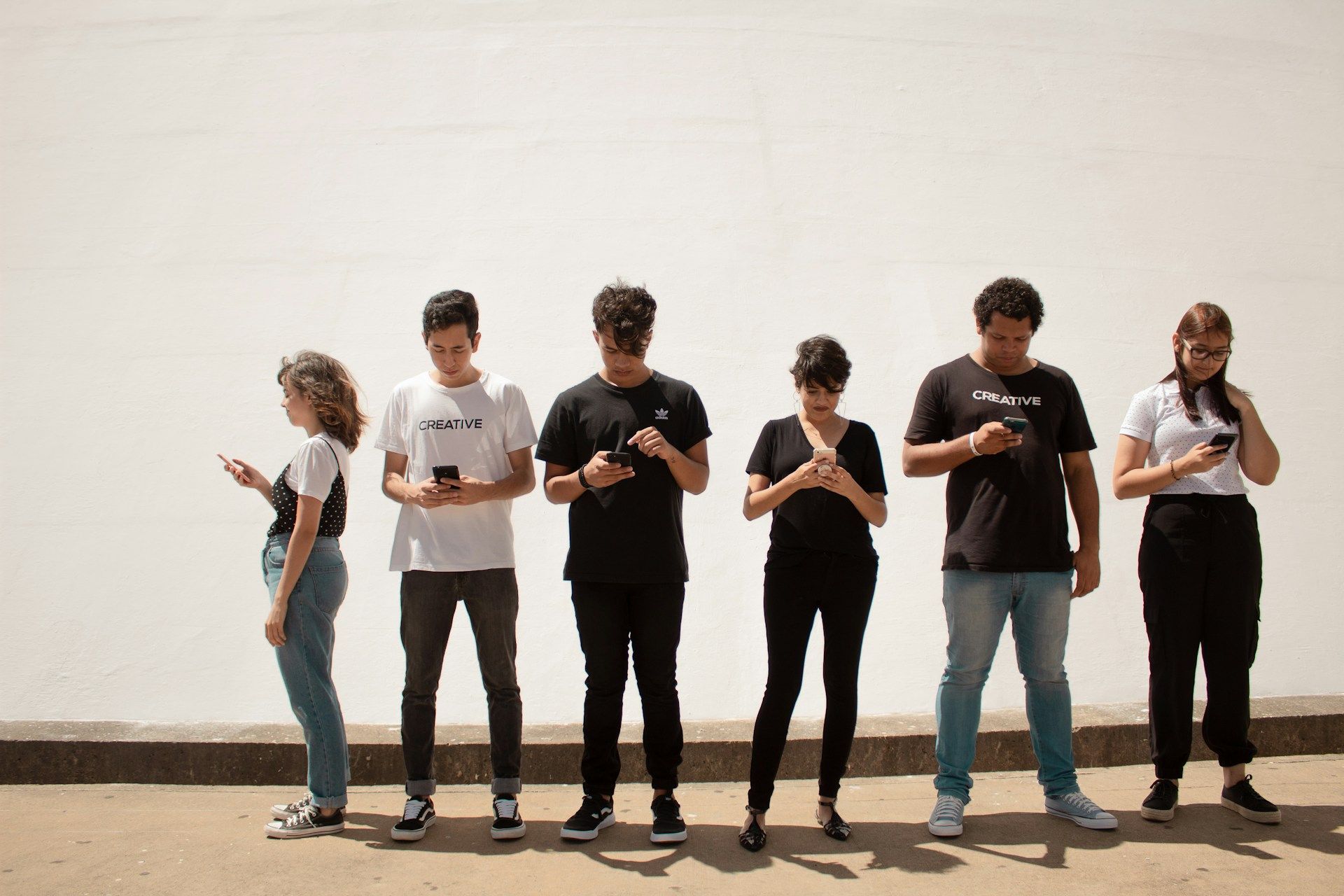 A group of people are standing next to each other looking at their phones.
