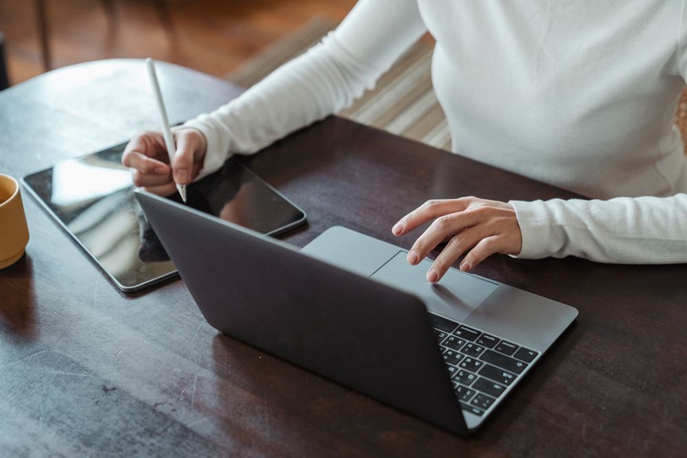 A woman is sitting at a table using a laptop and a tablet.