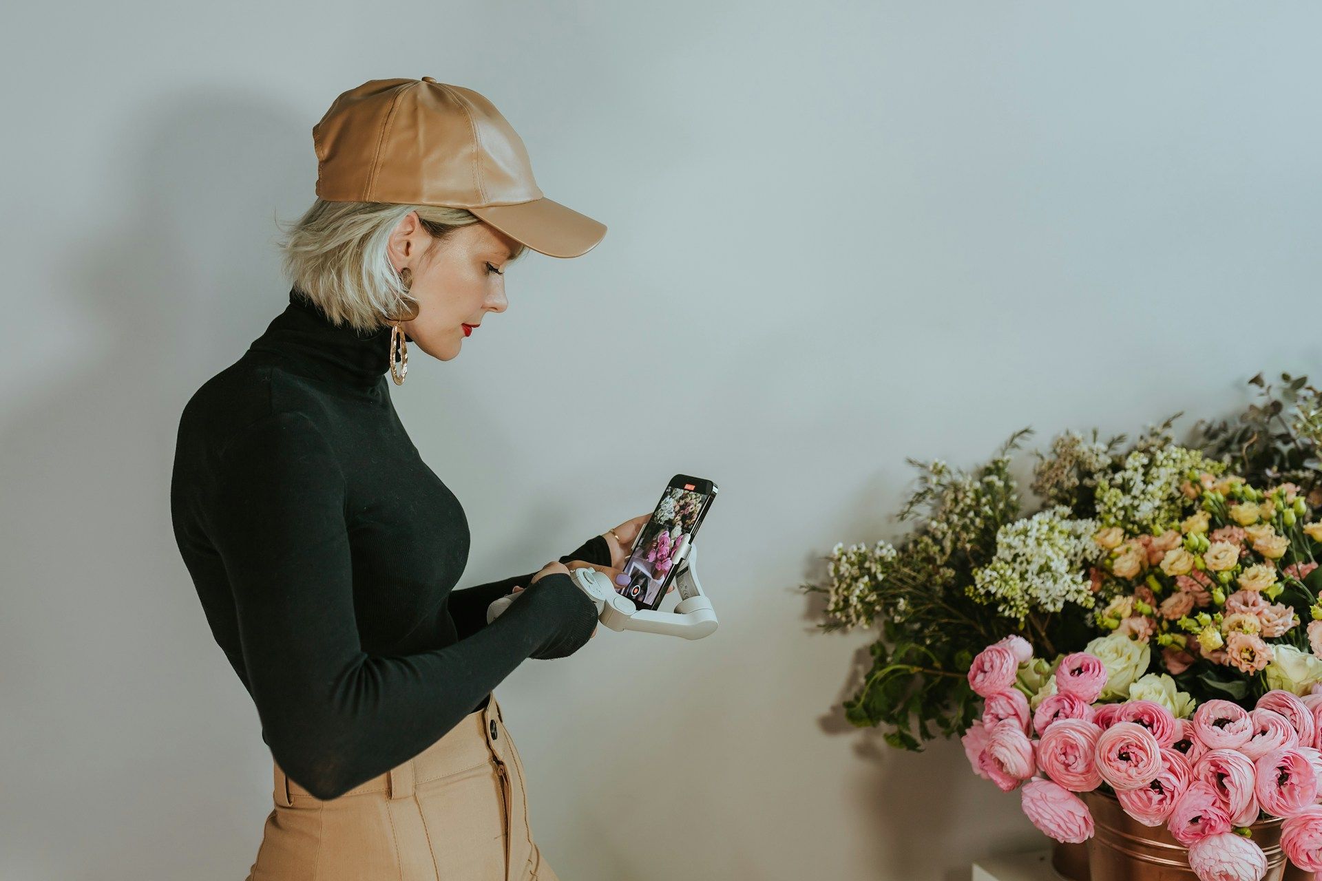 A woman is standing in front of a vase of flowers looking at a cell phone.
