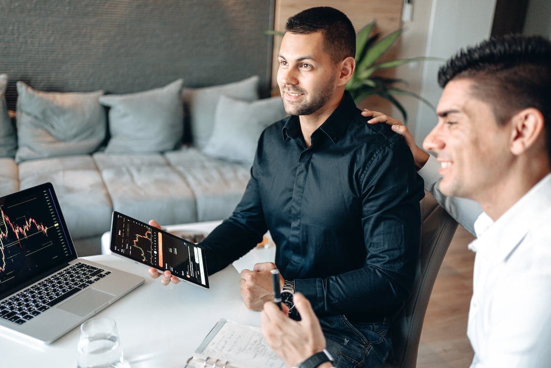 Two men are sitting at a table with a laptop and a tablet.