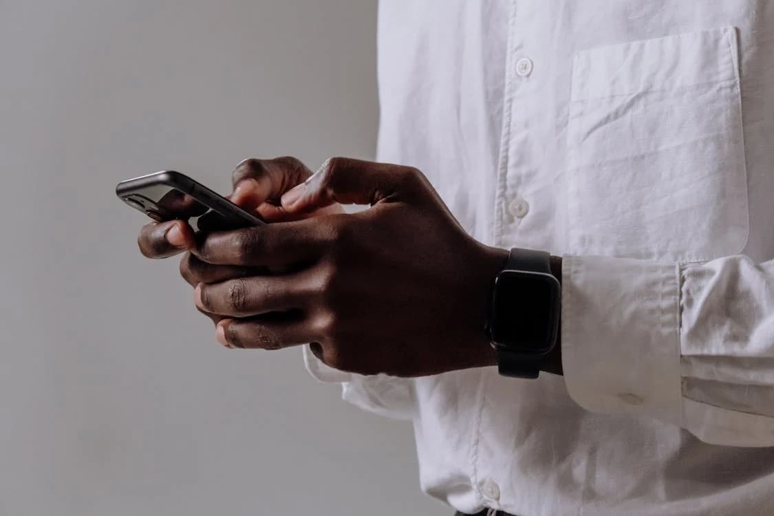 A man in a white shirt is holding a cell phone in his hands.