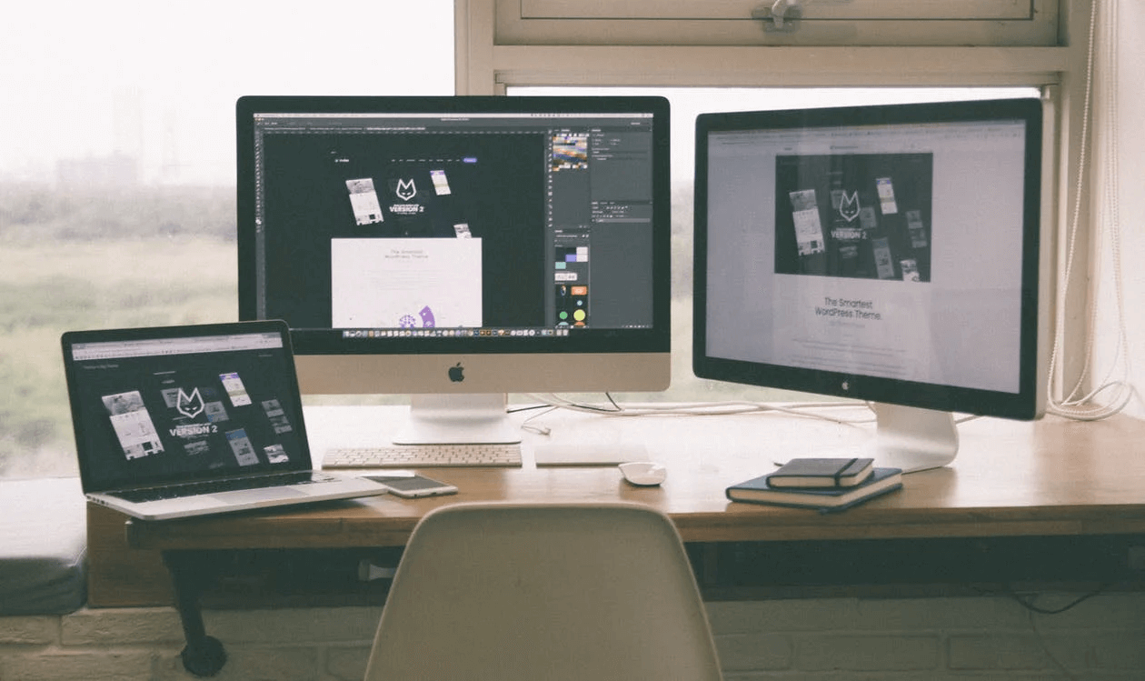 A desk with two computer monitors and a laptop on it.