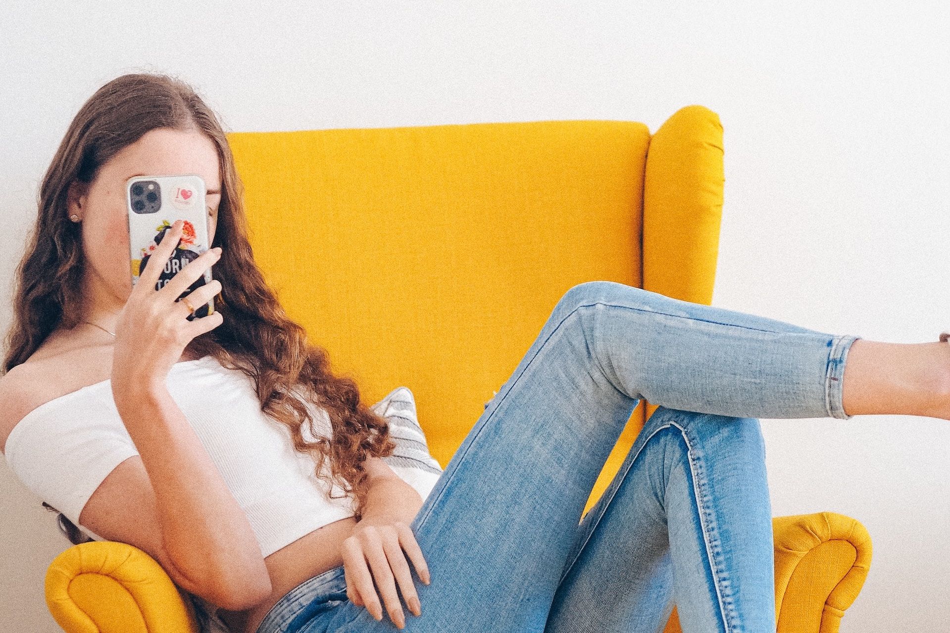 A woman is sitting in a yellow chair looking at her phone.