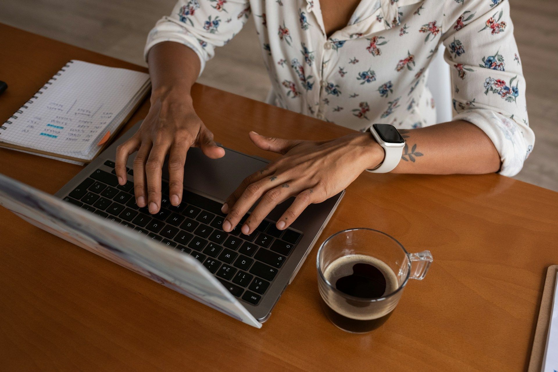 A woman is typing on a laptop computer at a desk with a cup of coffee.