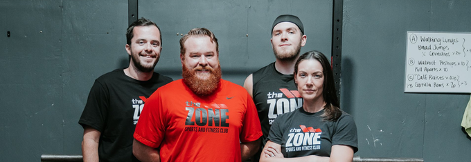 Four people in black and red shirts posing in front of a gray wall, smiling at the camera.