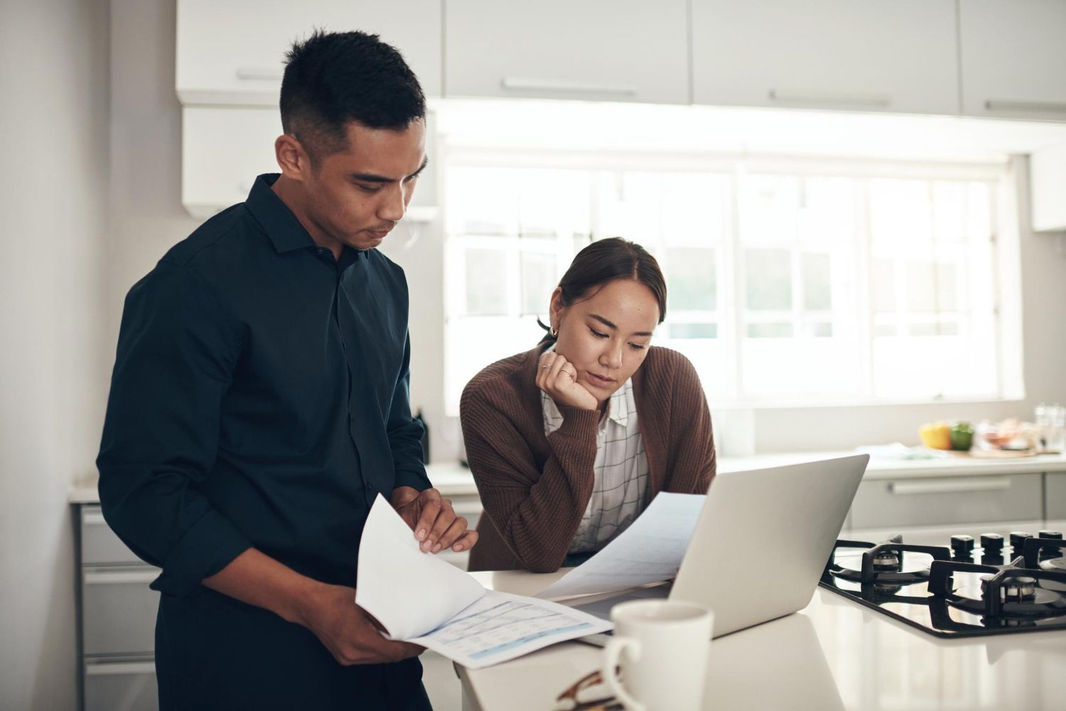 Two coworkers reviewing documents beside a laptop in a bright kitchen
