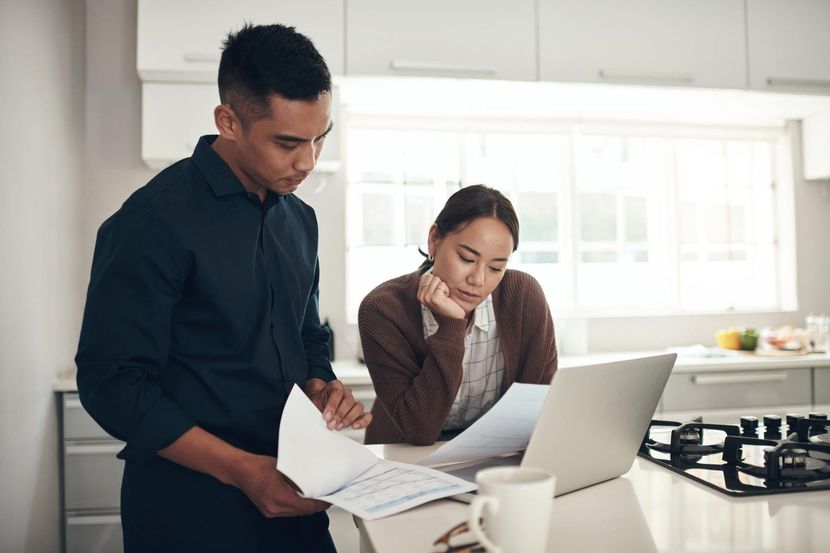 Two coworkers reviewing documents beside a laptop in a bright kitchen