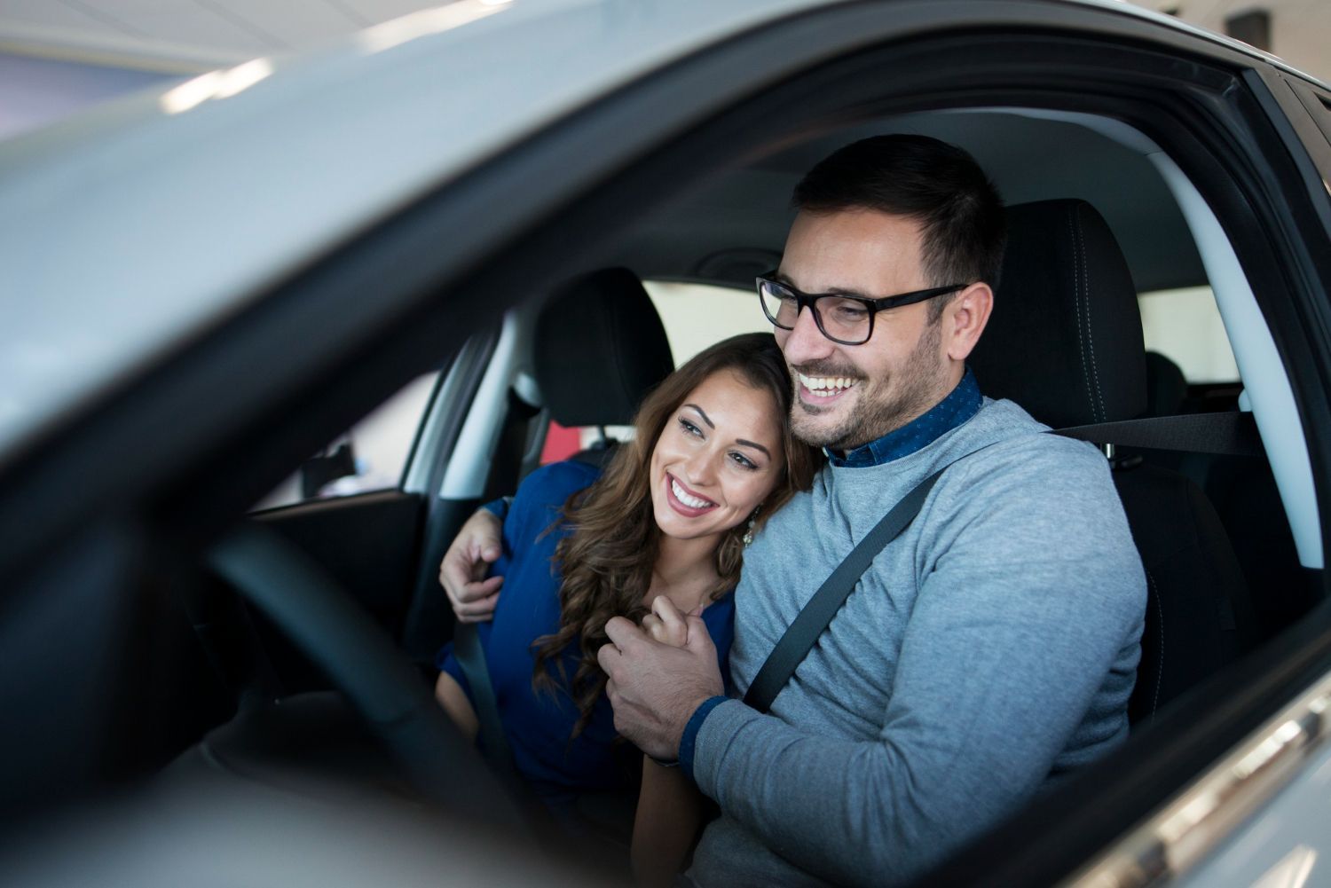 Couple smiling together inside a car, embracing in the front seat