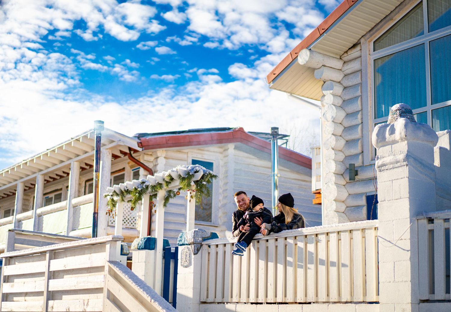 People sitting on a white porch beside colorful beach houses under a bright blue sky.