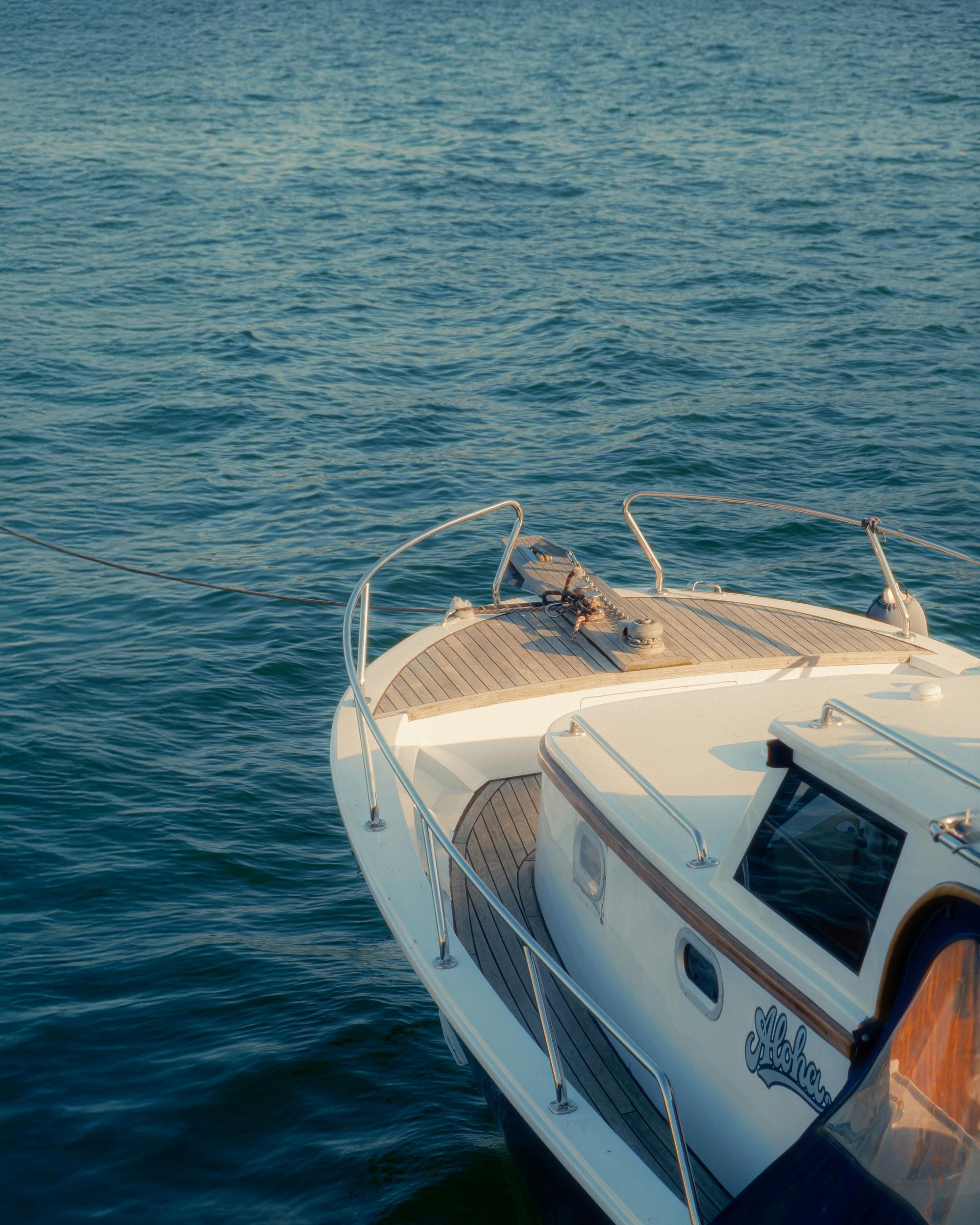 White boat bow on blue ocean, viewed from above, with deck rails and a small cabin roof visible.
