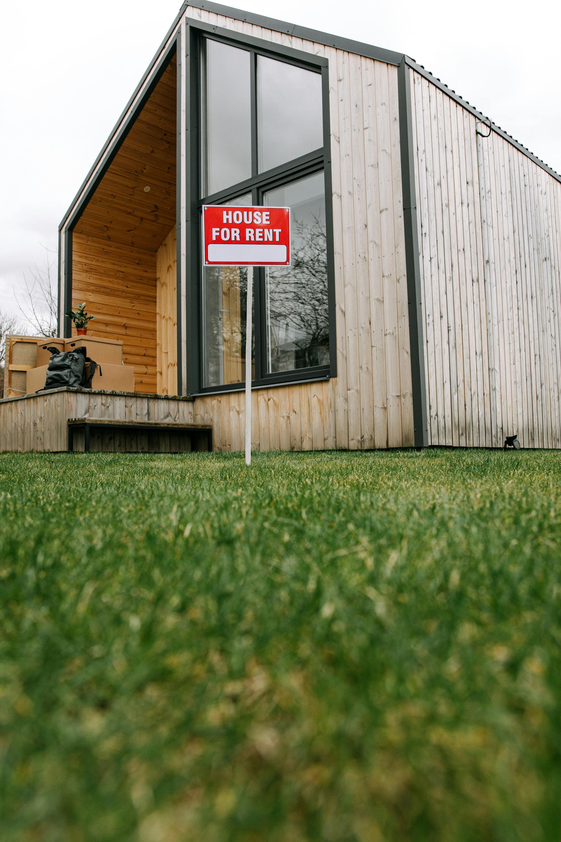 Modern tiny house with glass door and red “FOR SALE” sign on grassy lawn