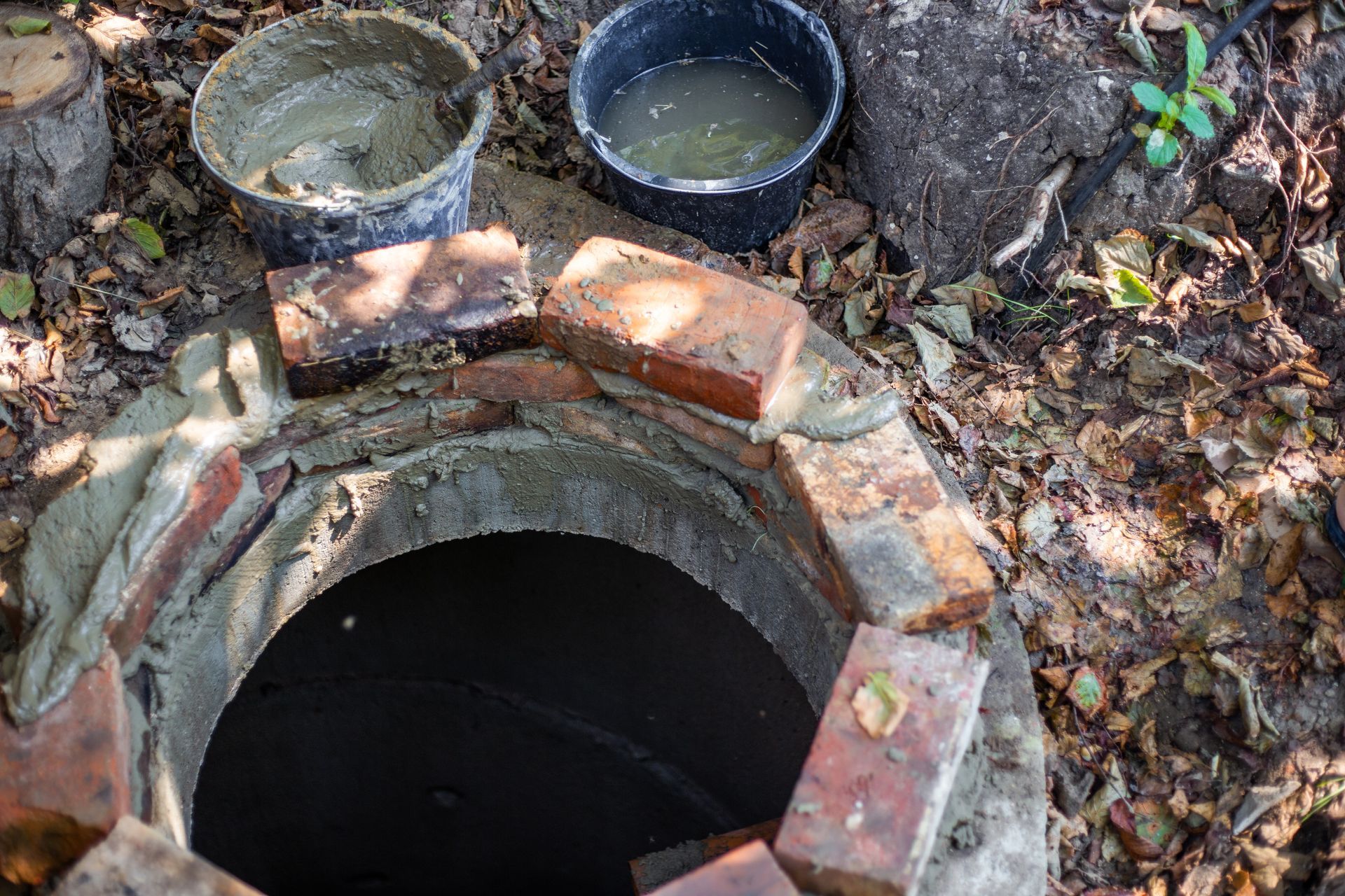 Bricks bordering a dark, circular opening. Buckets of mortar and water nearby.