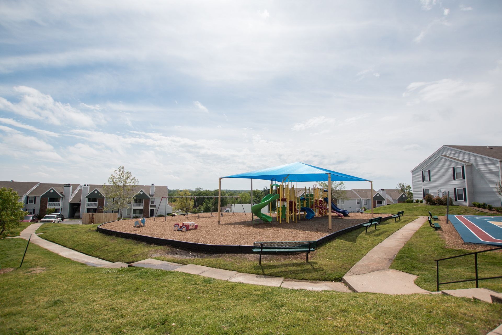 There is a playground with a blue umbrella in the middle of the park.