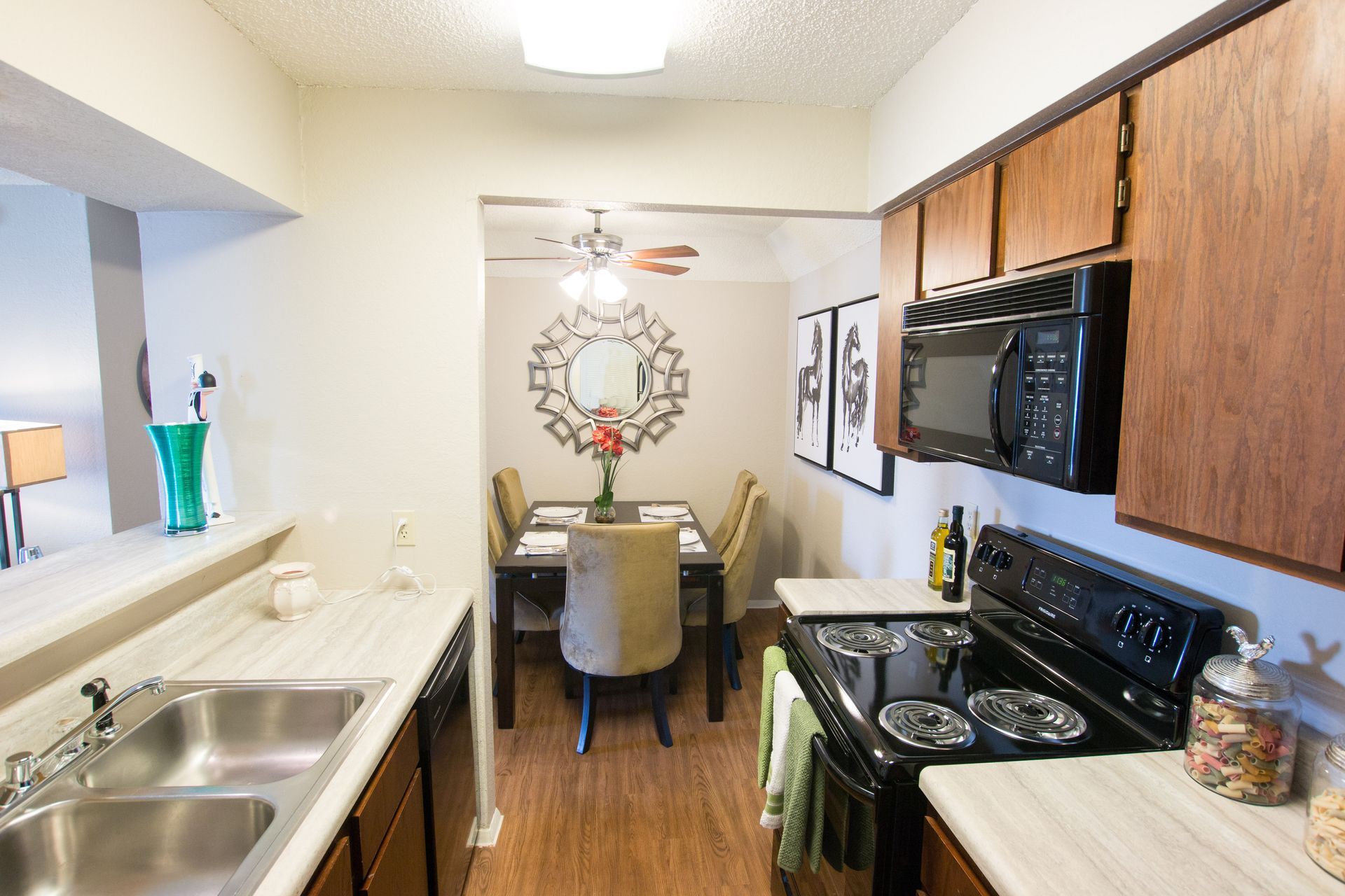 A kitchen with a sink , stove , microwave and a dining room in the background.