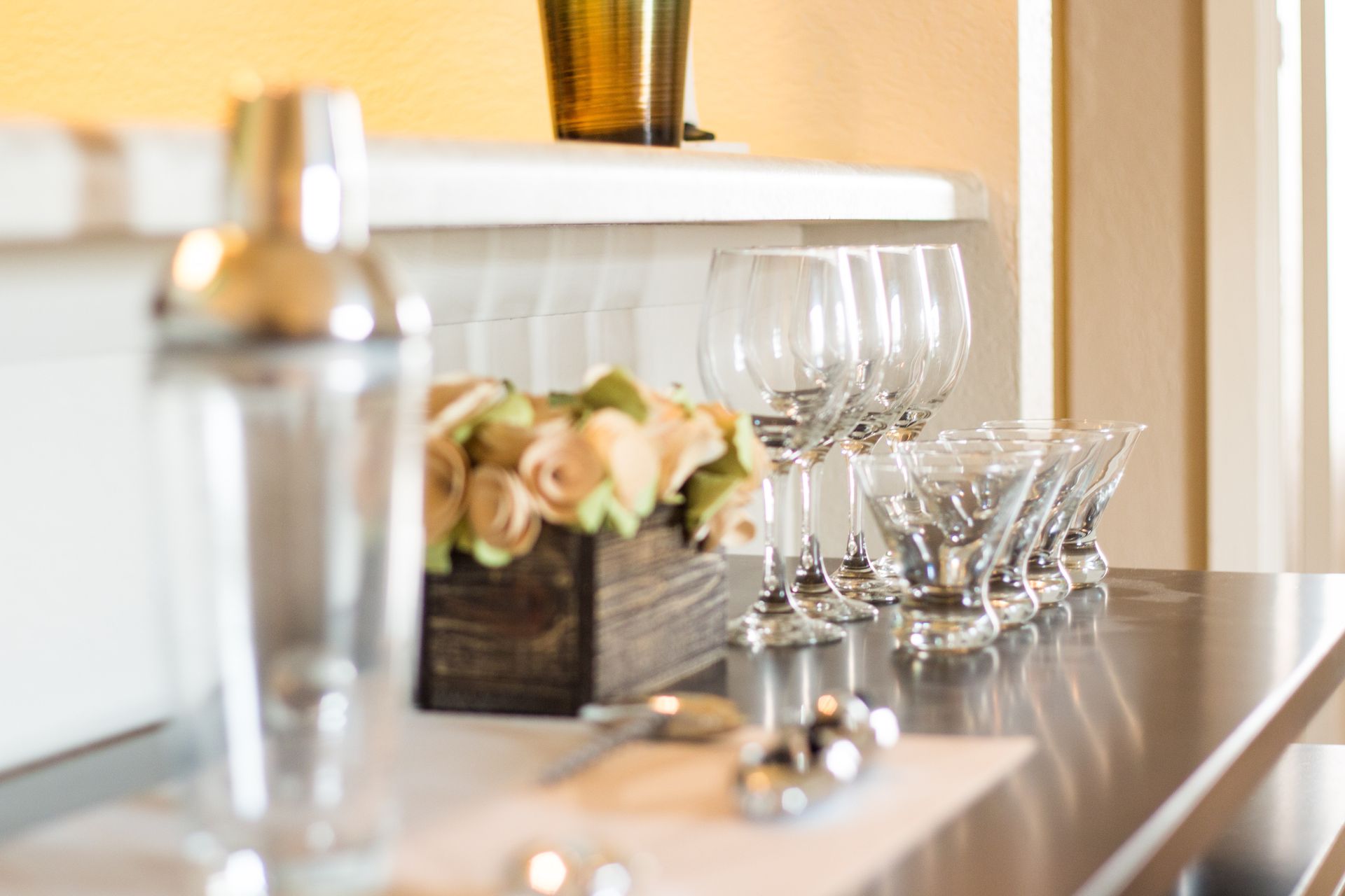 A row of wine glasses are lined up on a stainless steel counter.