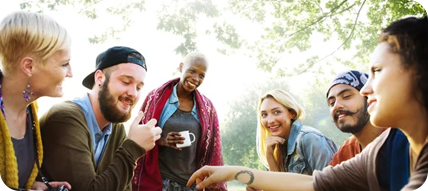 A group of diverse friends smiling and talking outdoors; sunny day.