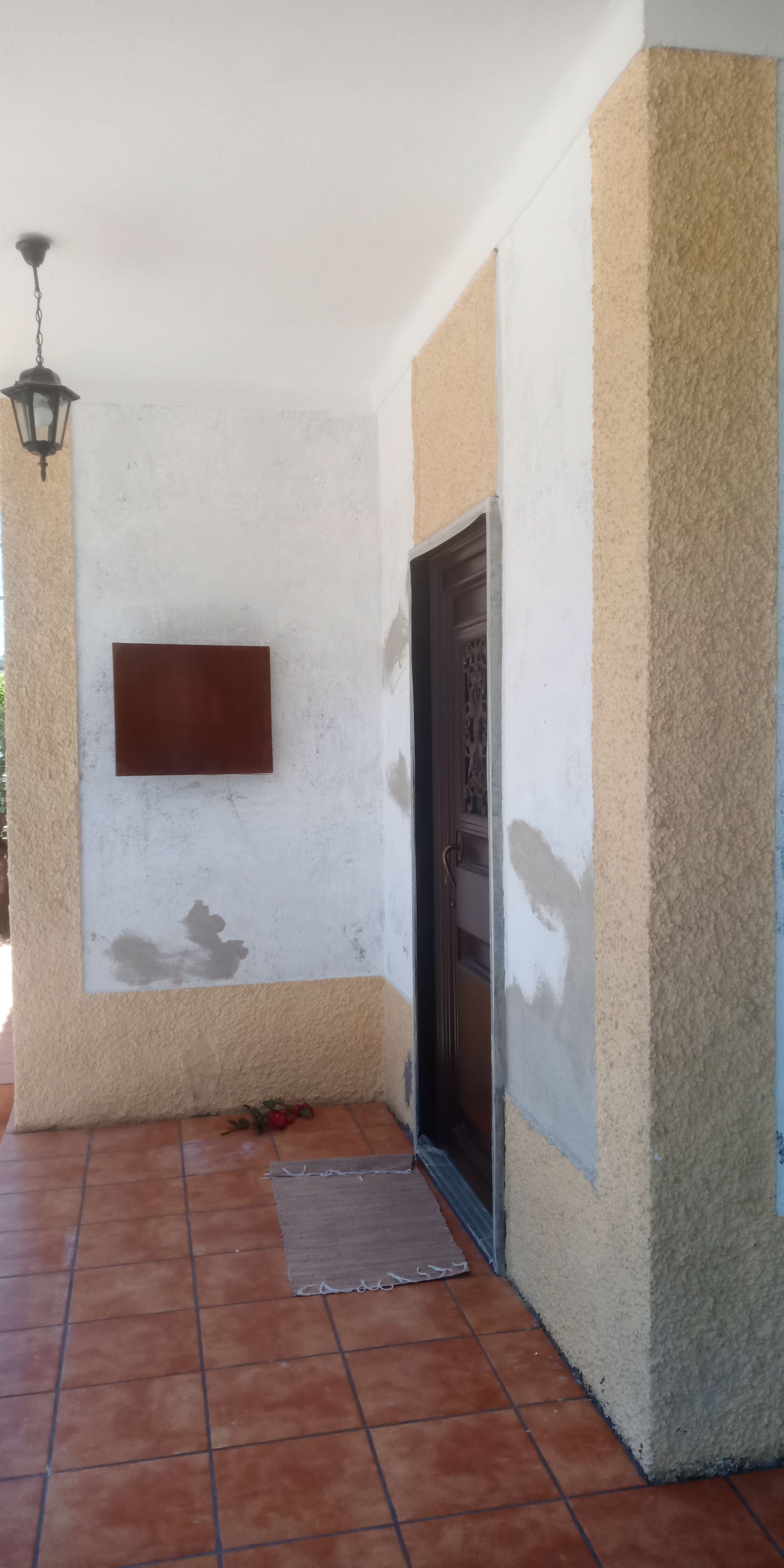 Varanda externa coberta com piso de azulejo marrom, teto branco e porta marrom.
